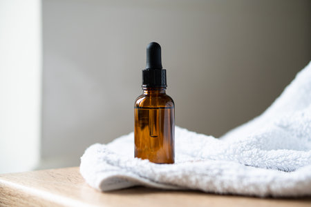 Amber glass serum oil dropper bottle and white towel on table mock-up, cosmetic container daylight shotの写真素材