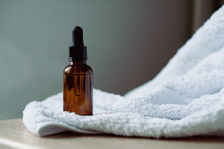 Amber glass serum oil dropper bottle and white towel on table mock-up, cosmetic container daylight shotの写真素材