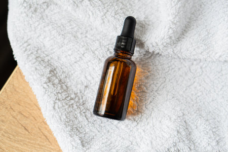 Amber glass serum oil dropper bottle laying on white towel mock-up, cosmetic container daylight shotの写真素材