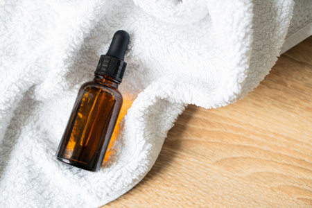 Amber glass serum oil dropper bottle laying on white towel mock-up, cosmetic container daylight shotの写真素材