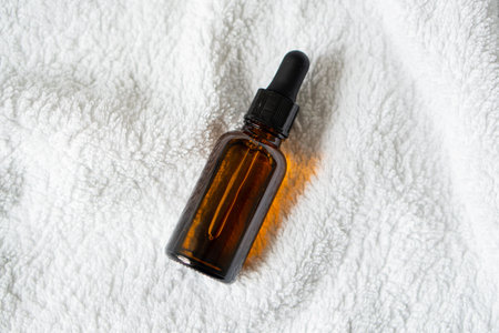 Amber glass serum oil dropper bottle laying on white towel mock-up, cosmetic container daylight shotの写真素材