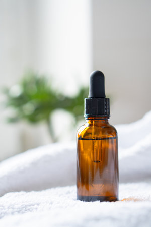 Brown amber glass serum oil dropper bottle and white towel on table mock-up, cosmetic container in real interiorの写真素材