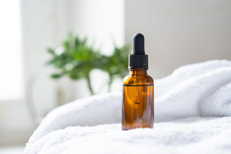 Brown amber glass serum oil dropper bottle and white towel on table mock-up, cosmetic container in real interiorの写真素材