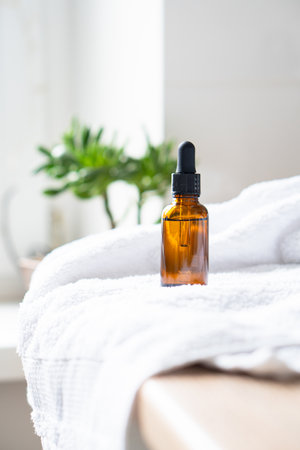 Brown amber glass serum oil dropper bottle and white towel on table mock-up, cosmetic container in real interiorの写真素材