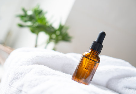 Brown amber glass serum oil dropper bottle and white towel on table mock-up, cosmetic container in real interiorの写真素材
