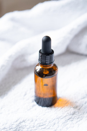 Amber glass serum oil dropper bottle and white towel on table mock-up, cosmetic container daylight shotの写真素材