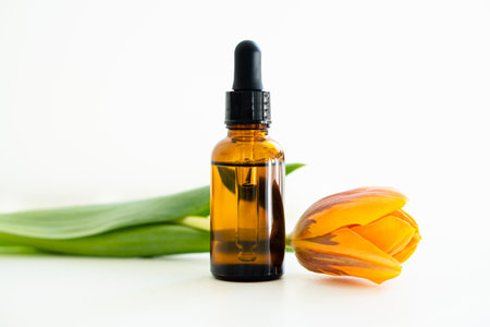 Amber glass cosmetic dropper bottle and orange tulips isolated on white background, serum bottle mockupの写真素材