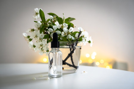Clear glass cosmetic dropper bottle and white cherry flowers with bokeh lights, care product mockupの写真素材