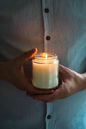 Man holding a burning candle in his hands, elegant young man with candle jar, meditation and mindfulness conceptの写真素材