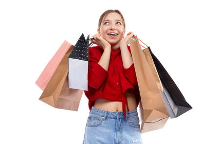 Young beautiful smiling girl in red sweetshot and blue jeans with paper bags for shopping happy...