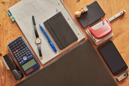 High angle shot of a work desk with office equipment. Office equipment on a wooden vintage table. Desk with laptop, smartphone, calculator, puncher, forklift, notebook.の写真素材