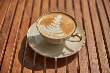 Close up of a cappuccino with latte art on a wooden table. Cappuccino in the sun.の写真素材