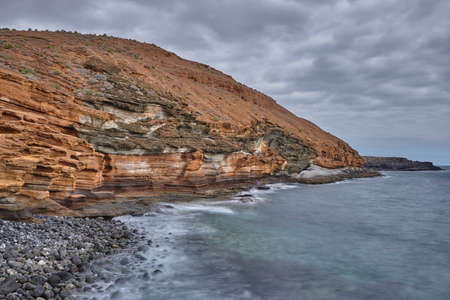 Long exposure of red cliffs close to el Medano, Tenerife. Red cliffs along the coastline of Tenerife, Canary Islands. Red lava rocks along the coastline of Tenerife.の写真素材