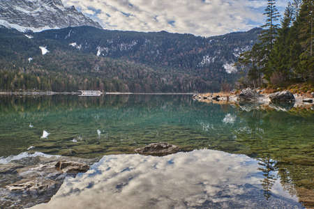 Reflecting mountain lake in the german alps. Eibsee in bavaria. Turquoise mountain lake in front of snowy mountain peaks.の写真素材