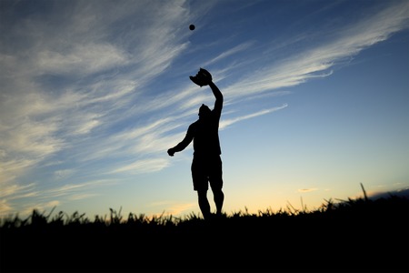 A man silhouetted by the sunset is just beginning catch ball with gloveの写真素材