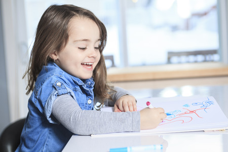 Cheerful little girl colouring at the table at home in kitchen