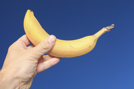 A hand holding banana outside with sky viewの写真素材