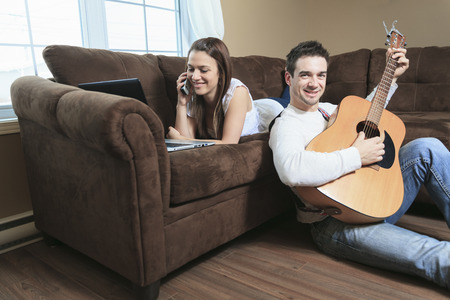 A Handsome man serenading his girlfriend with guitar at home in the living roomの写真素材
