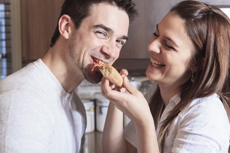 A Happy young couple eating pizza at the kitchenの写真素材