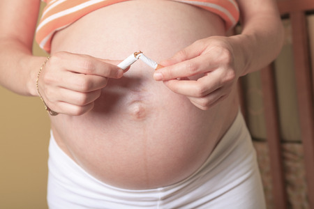 Young pregnant woman holding cigarette on baby room