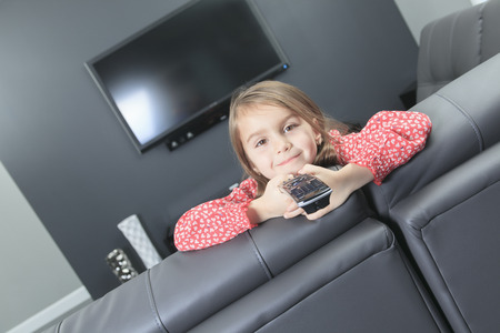 A cute little girl with remote control in front of TV.の写真素材