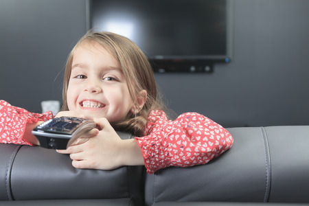 A cute little girl with remote control in front of TV.の写真素材