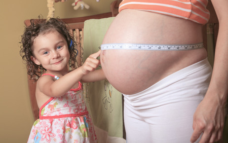 Little cute girl looking at her mother pregnant tummyの写真素材