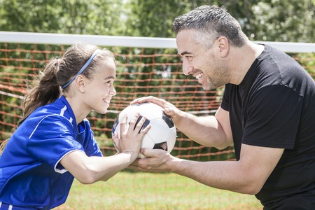A teenager girl with his father play soccer in a beautiful dayの写真素材