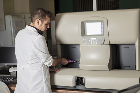 A scientist at work in a laboratory close to a blood test machine.