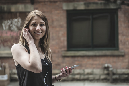 A young beautiful woman in town listening music earphoneの写真素材