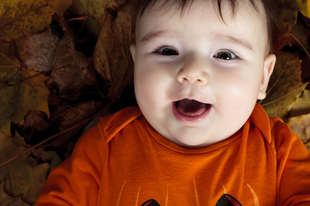 Sweet laughing baby girl playing with a huge pumpkin wearing a knitted pumpkin hat on white backgroundの写真素材
