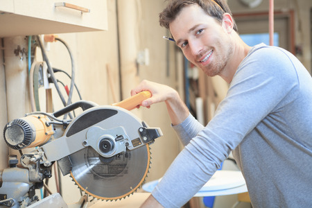 A carpenter working hard at the workshop with saw.