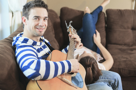 A Handsome man serenading his girlfriend with guitar at home in the living roomの写真素材