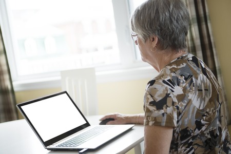 A senior woman working on her laptop in her kitchen tableの写真素材