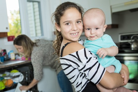 A family in kitchen with baby holding by his sisterの写真素材