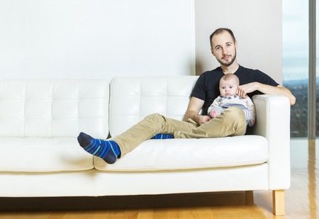 A father with baby on the sofa taking good timeの写真素材