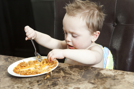 Adorable little boy eating pasta indoor. Toddler child in domestic kitchen or in nursery. Cute kid and healthy food.の写真素材