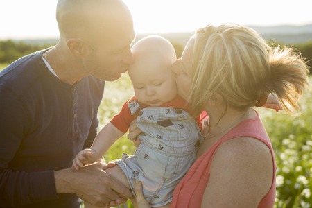 An happy family of three. Father, mother and baby playing outside in summer at sunset time.