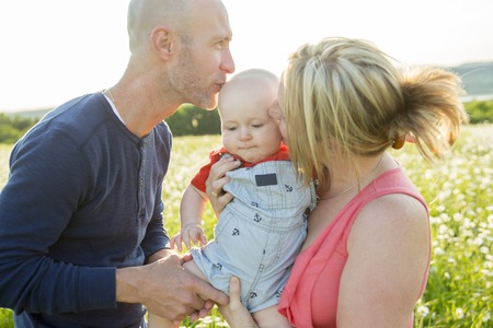 An happy family of three. Father, mother and baby playing outside in summer at sunset time.