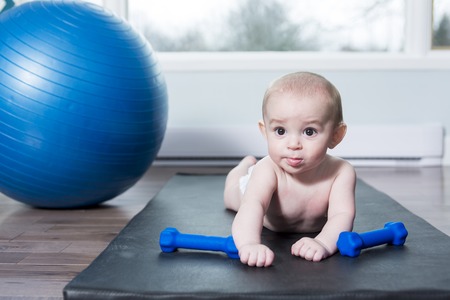 A cute baby doing exercises with ball at homeの写真素材