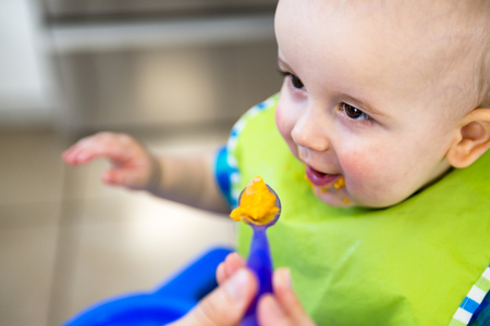 A Mother feeding hungry baby in the highchair indoors
