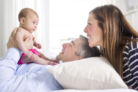 Two Parents Cuddling Newborn Baby In Bed At Home