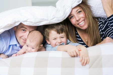 A Photo of loving family of four lying on white bed in morning.