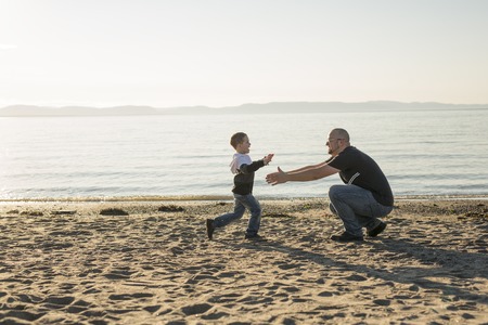 A Son on father shoulders at the beach having fun at sunset togetherの写真素材