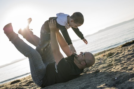 A Son on father shoulders at the beach having fun at sunset together