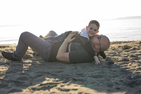 A Son on father shoulders at the beach having fun at sunset togetherの写真素材