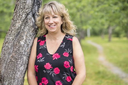 A Woman outdoors smiling close to a tree in the forest