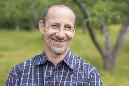 A Men outdoors smiling close to a tree in the forest
