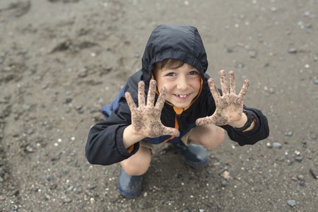 A boy enjoying the rain and having fun outside on the beach on a gray rainy