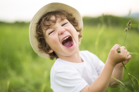 Portrait of adorable kid boy with hat standing on a summer meadowの写真素材